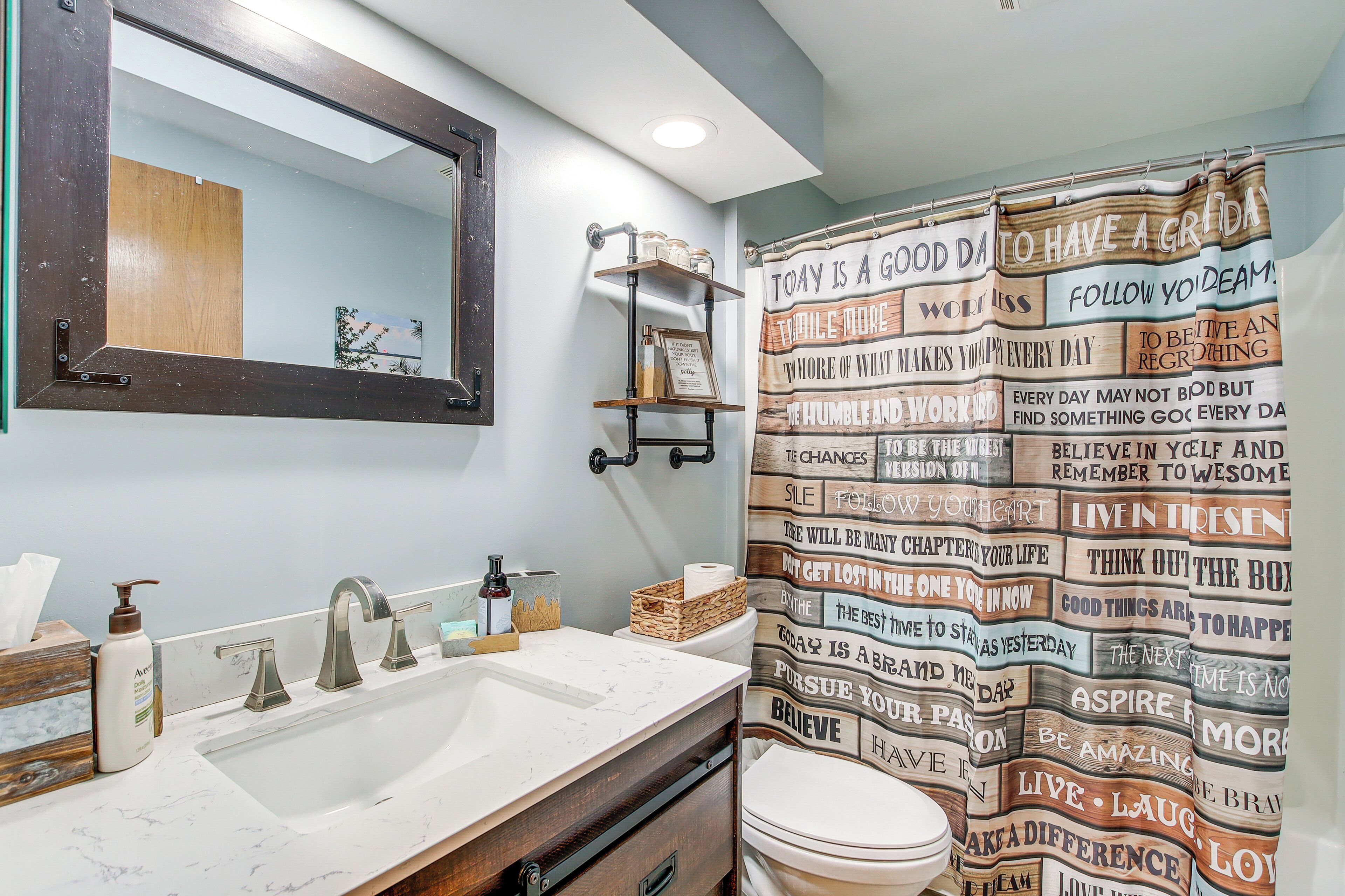 Un baño con un espejo grande, un lavabo con encimera de mármol y una cortina de ducha con citas motivacionales.