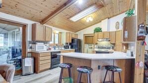 A spacious kitchen with wooden cabinets, a central island with stools, and a large window providing natural light. - Versatile Castle Rock Lake Home With Fire Pit! (Friendship)