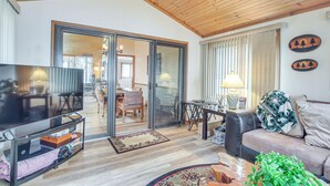 A modern living room with a wooden ceiling, a flat-screen TV, a sofa, a coffee table, and a large mirror reflecting the dining area. - Versatile Castle Rock Lake Home With Fire Pit! (Friendship)