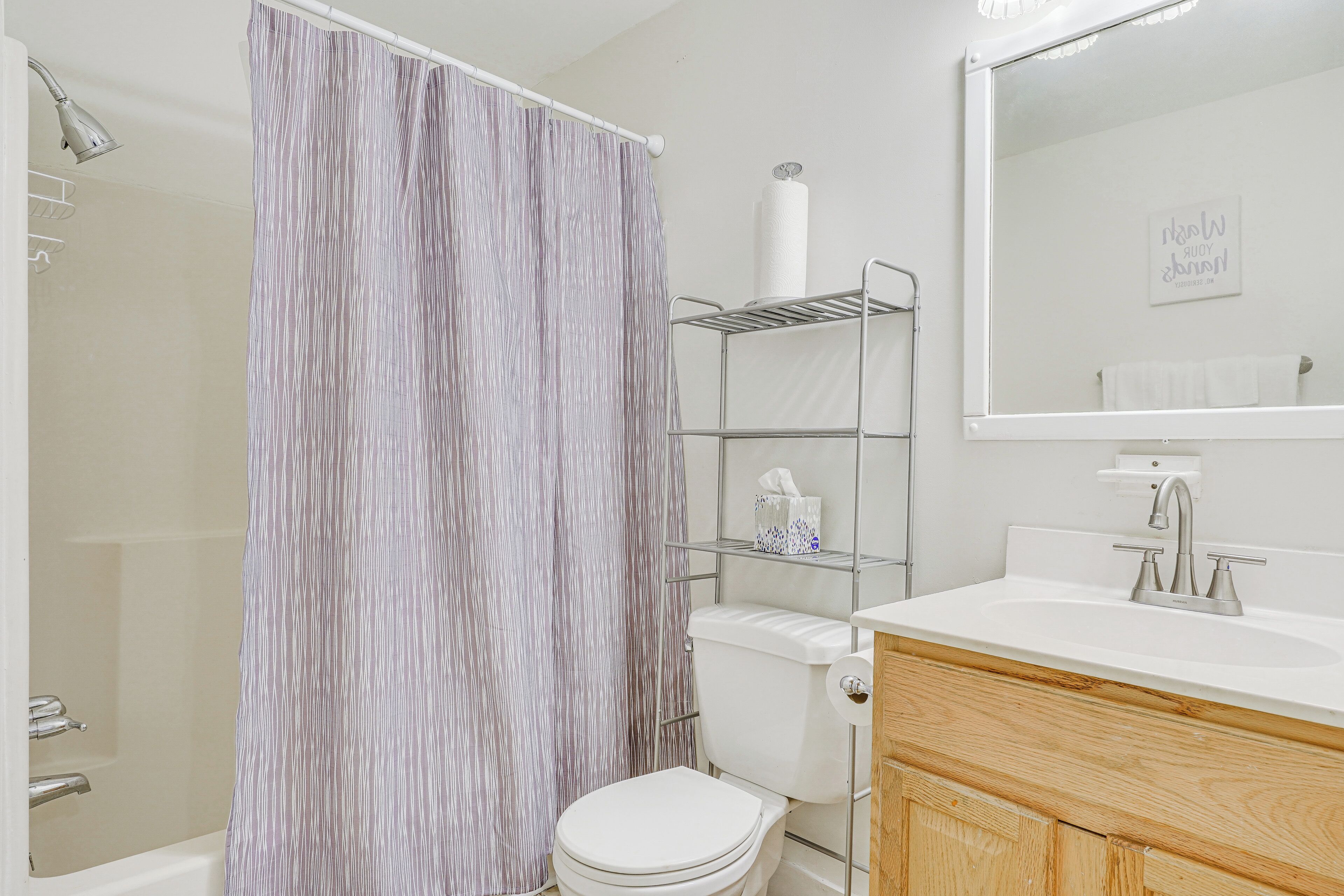 A bathroom with a shower curtain, a toilet, a sink with a mirror, and a shelf with toiletries.