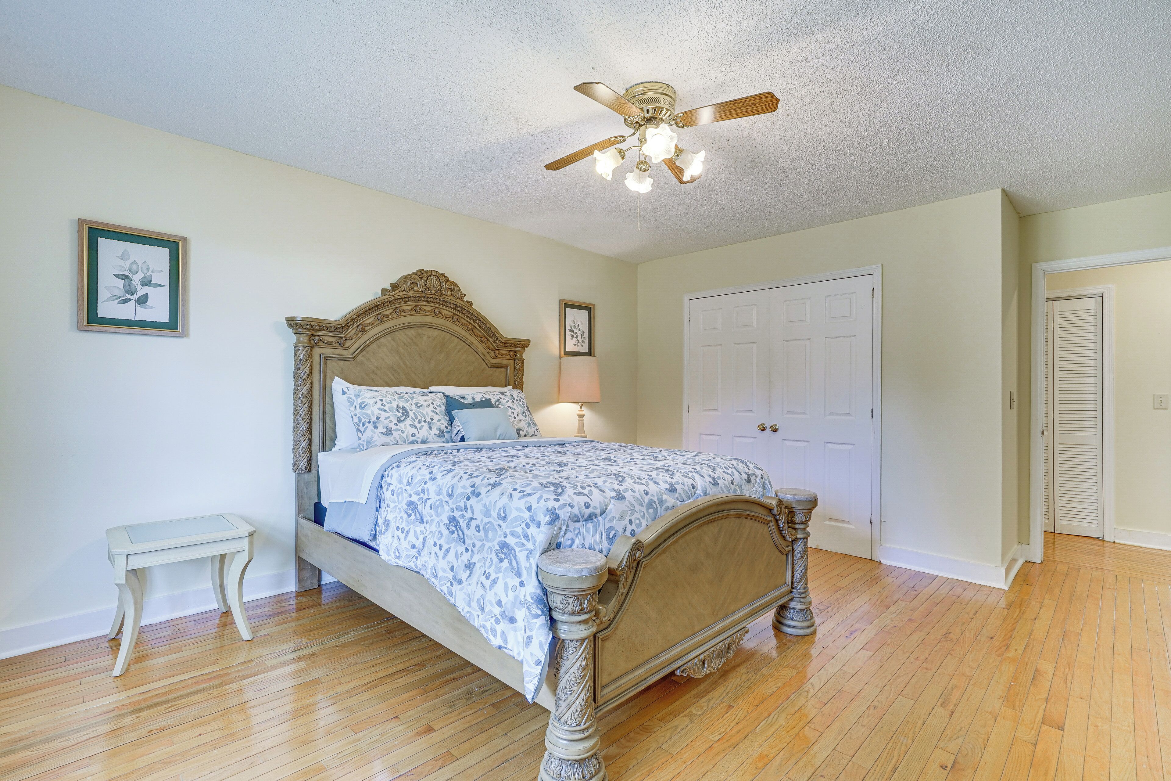A bedroom with a wooden bed, a nightstand, a ceiling fan, and a door.
