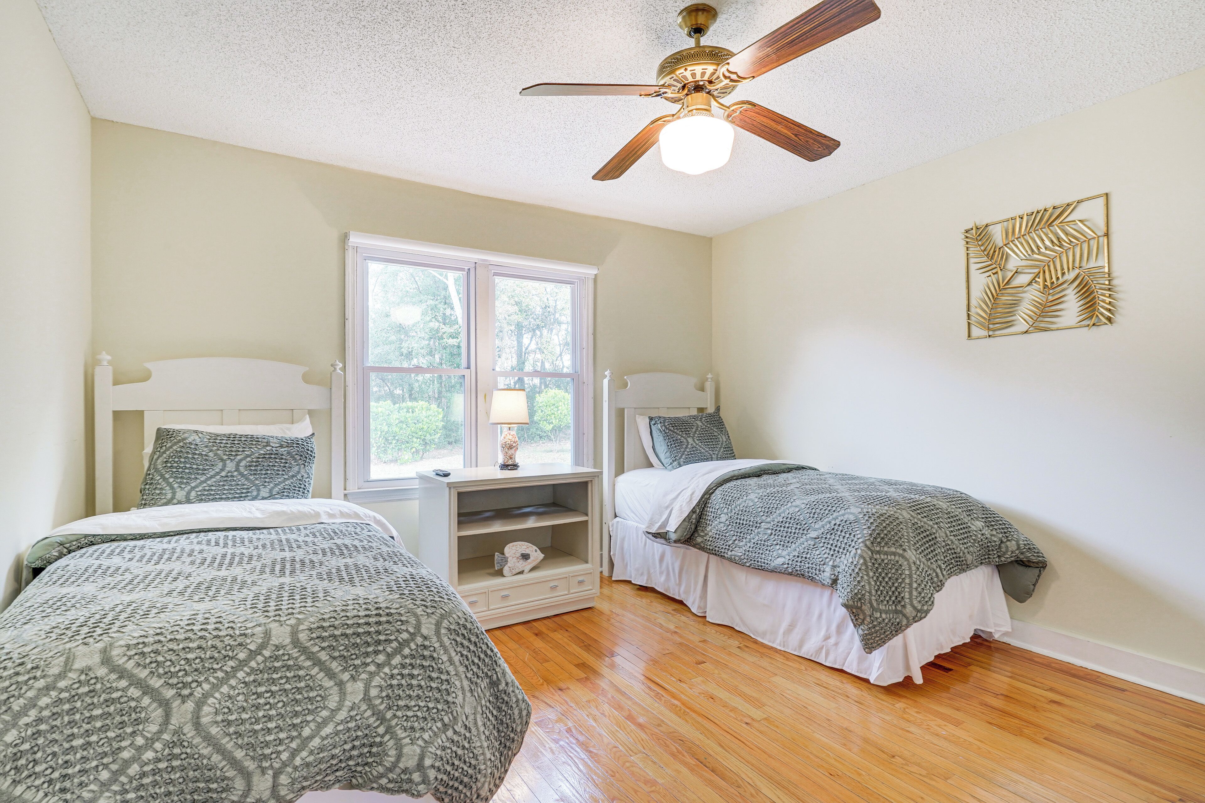 A bedroom with two beds, a ceiling fan, a window, and a decorative wall piece.