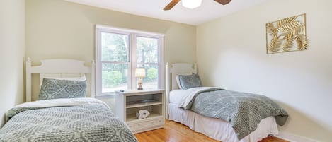 A bedroom with two beds, a ceiling fan, a window, and a decorative wall piece.