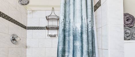 Een douche met een blauw douchegordijn, een handdoekhouder aan de muur en een betegeld douchegedeelte.