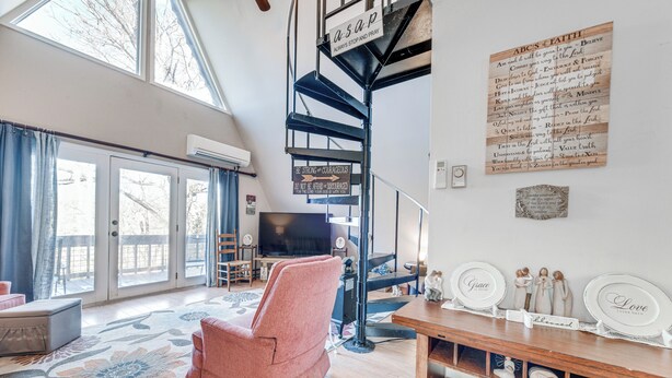 Un salon spacieux avec une grande fenêtre, un fauteuil rose, une table basse en bois et un escalier agrémenté d’une pancarte.
