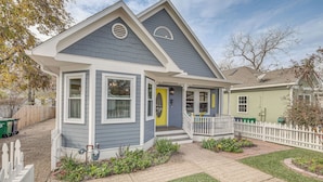 A two-story house with a grey and white exterior, a yellow front door, and a small porch with a white picket fence. - Brenham Rental w/ Deck & Yard < 1 Mi to Downtown! (Brenham)