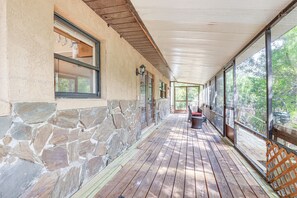 A covered porch with stone walls and wooden flooring, large windows, and a view of trees. - Lake Placid Home w/ Screened Porch: Near Lake Clay (Lake Placid)