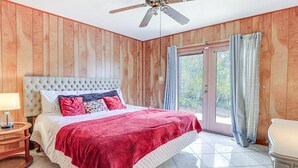 Un dormitorio con una cama grande, paneles de madera en las paredes, un ventilador de techo y un ventanal corredero que da a un balcón.