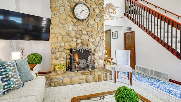 Uma sala de estar com lareira de pedra, televisão de tela plana, escada e sofá moderno.