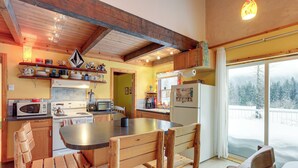 A kitchen with wooden furniture, a dining table, and a view of a snowy landscape through a large window. - Snoqualmie Pass Cabin w/ Deck: Walk to Ski Lift (Snoqualmie Pass)