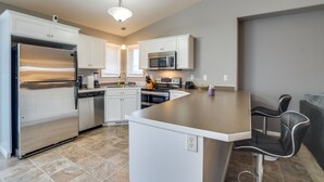 A modern kitchen with stainless steel appliances, white cabinetry, and a central island with bar stools. - Pet-friendly North Dakota Escape w/ Fenced-in Yard (West Fargo)