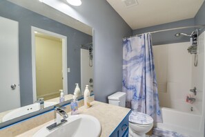 Une salle de bain équipée d’un lavabo, d’un miroir, de toilettes, d’une douche et d’un rideau de douche bleu.