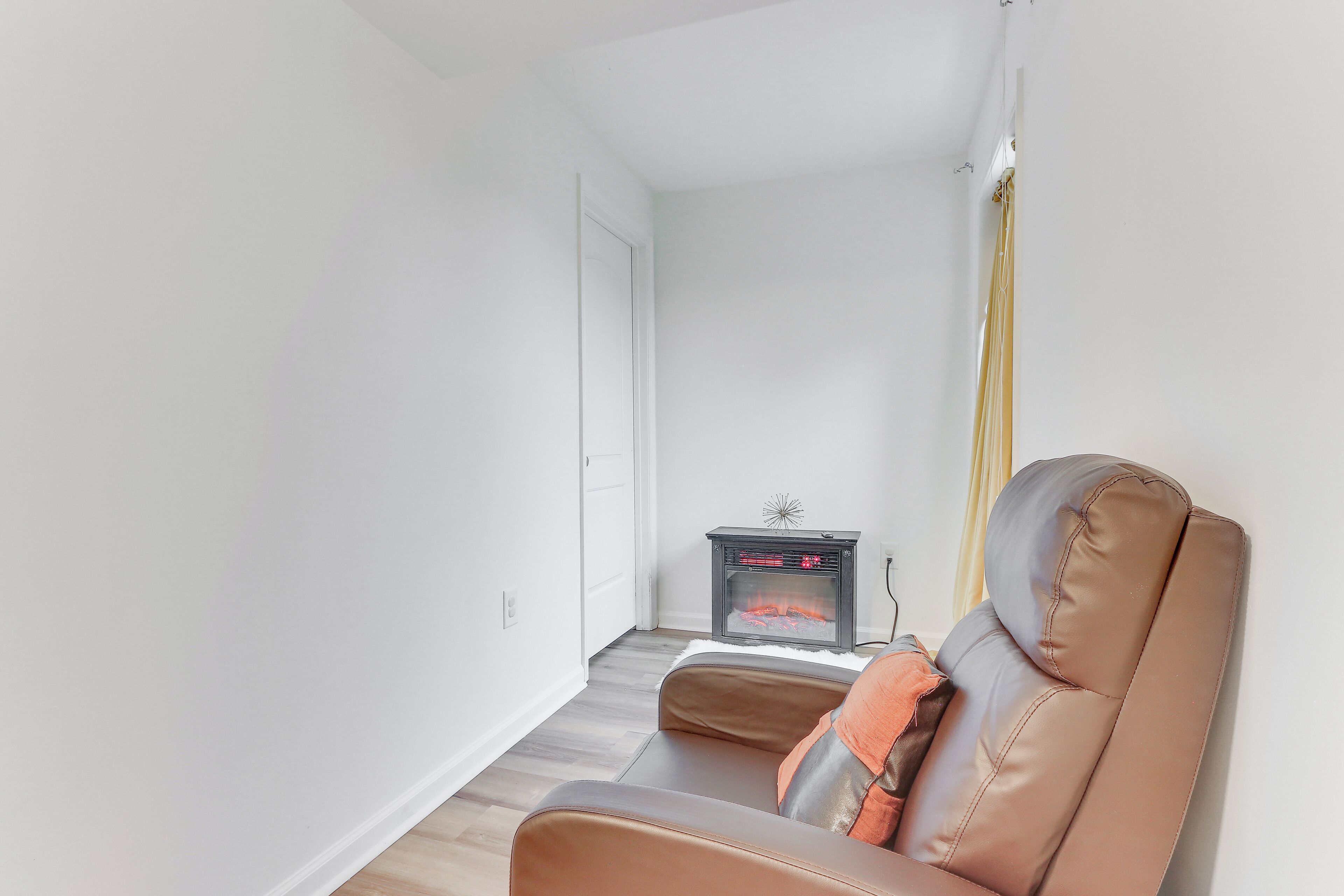 A living room with a brown leather sofa, a small black heater, and a white door.