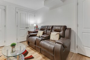 A modern living room with a brown leather sofa, a glass coffee table with a plant, and a red and brown patterned rug.