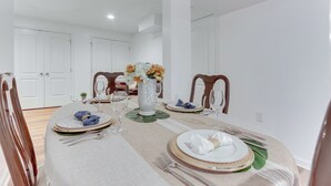 A dining area with a round table set for six, white walls, and wooden chairs. - Cozy Inwood Apartment: History, Hiking & Wine! (Inwood)