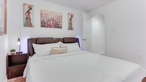 A bedroom with a large bed, a nightstand with a lamp, and three wall-mounted artworks. - Cozy Inwood Apartment: History, Hiking & Wine! (Inwood)