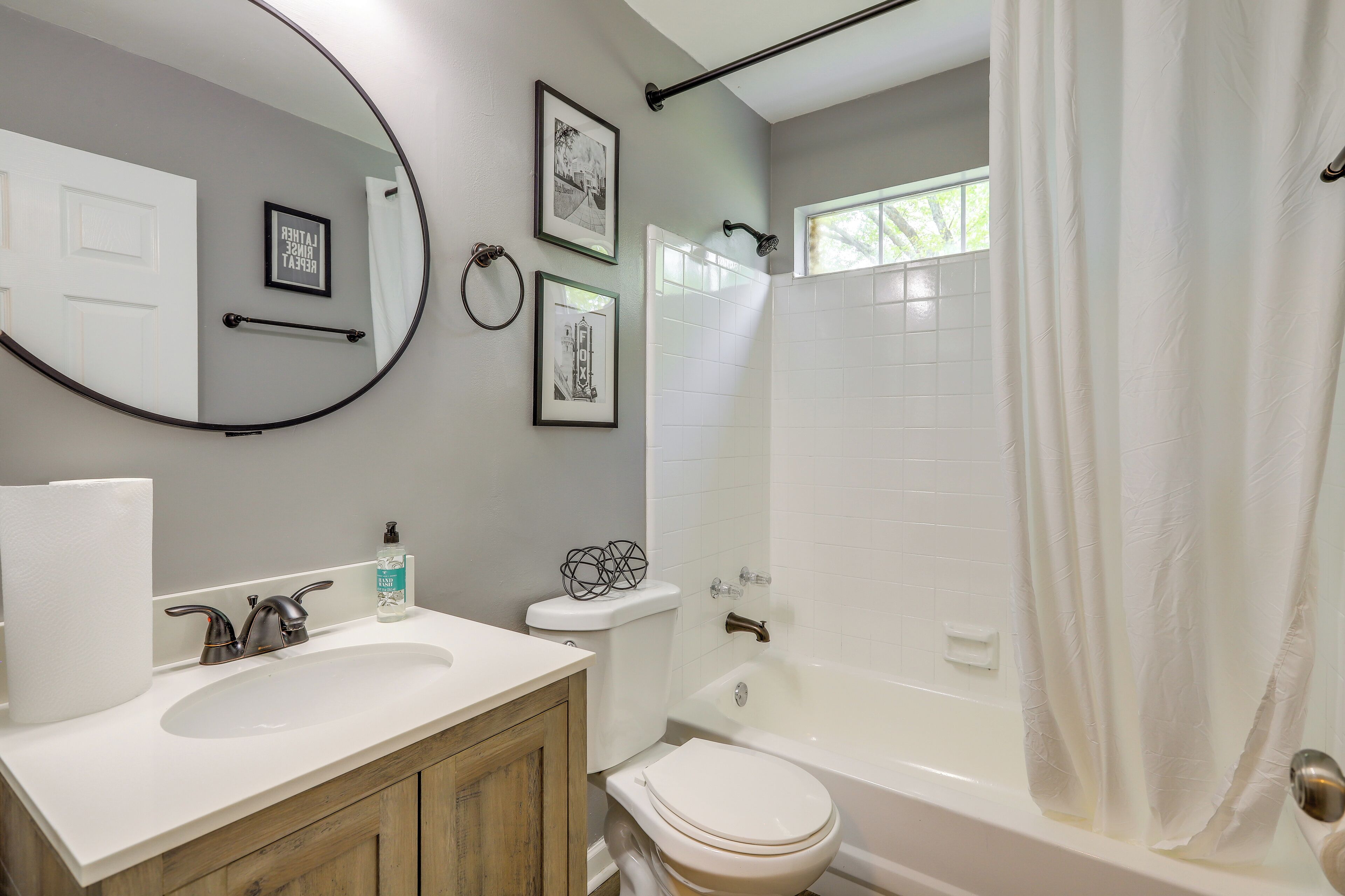 A bathroom with a white sink, toilet, and bathtub. There are framed pictures on the wall and a towel rack.