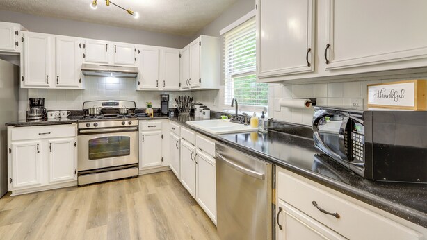 A kitchen with white cabinets, stainless steel appliances, a black countertop, and a ceiling light fixture. - Decatur Vacation Rental w/ Fenced Yard! (Decatur)