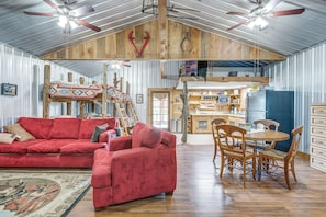 Une piÚce spacieuse avec un canapé rouge, une table à manger en bois avec des chaises, un ventilateur de plafond et un coin cuisine.