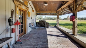 Ein überdachter Patio-Bereich mit Backsteinboden, Sitzgelegenheiten im Freien und Blick auf eine Wiese.