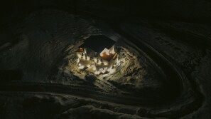 A cave with a small illuminated structure inside, possibly a cave dwelling or a tourist attraction.