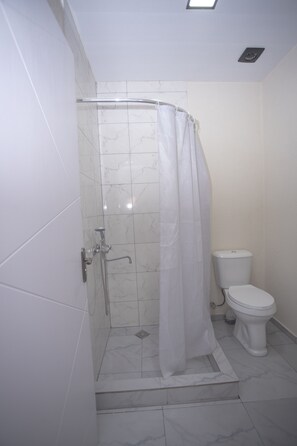 A bathroom with a shower, toilet, and white tiled walls.