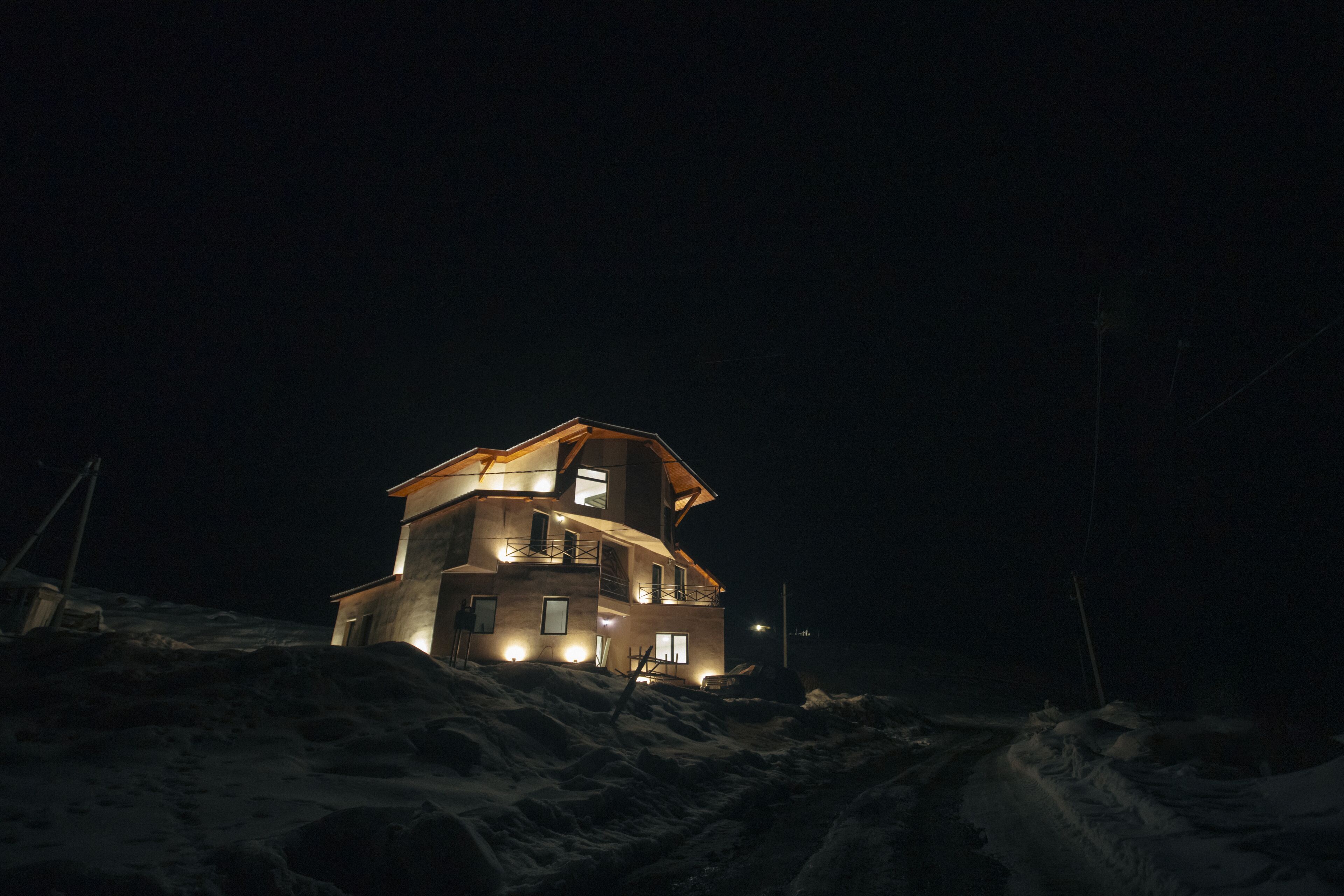 Un edificio de varios pisos con ventanas iluminadas y techo inclinado, rodeado de nieve.