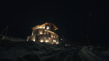 Un edificio de varios pisos con ventanas iluminadas y techo inclinado, rodeado de nieve.