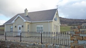A two-story house with a stone wall and a metal fence in front. - Harefield Holiday Home (Carrick)