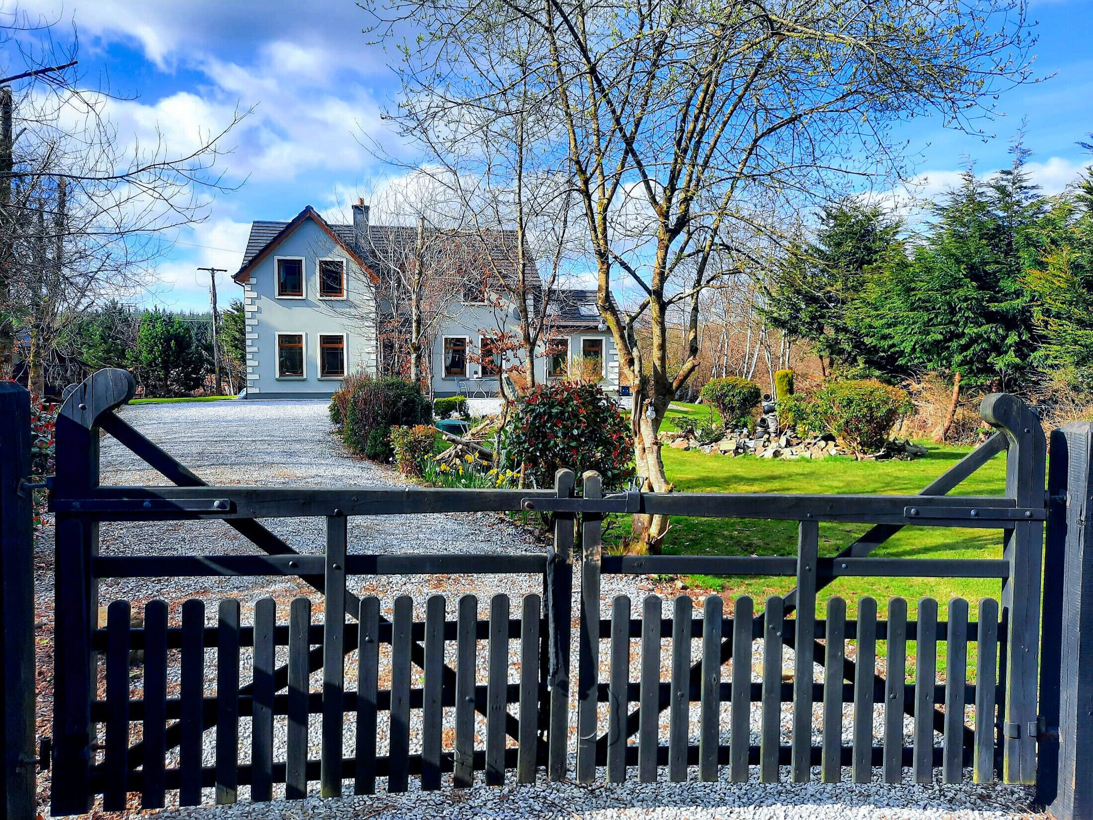 A two-story house with a gravel driveway leading to a wooden gate.