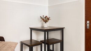 Eine Hausecke mit weißer Wand, einer Holztür und einem kleinen Tisch mit einem Blumenstrauß.