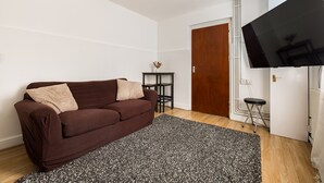 Ein Wohnzimmer mit braunem Sofa, einem schwarz-weißen Teppich, einer roten Hängeleuchte, einem Fernseher und einer Holztür.