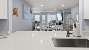 A modern kitchen with a white countertop, stainless steel sink, and a dining area with white chairs and a table.