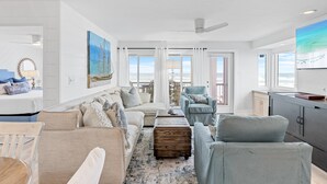 A spacious living area with a sofa, armchairs, and a coffee table. There is a large window with a view of the ocean.