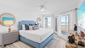 A bedroom with a bed, nightstands, a dresser, a ceiling fan, and a large window with a view.