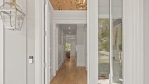 Un couloir doté d’un plancher en bois, de murs blancs et d’une porte en verre donnant sur un espace extérieur.