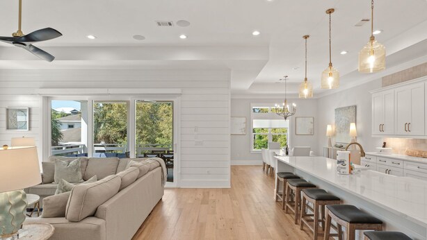 Une cuisine moderne avec des meubles blancs, un îlot central doté de tabourets et des luminaires suspendus.