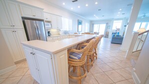 A spacious kitchen with white cabinetry, a central island with bar stools, and a large window providing natural light. - Dog-Friendly, Pool & Tennis Court, Hot Tub in Sunset Beach! (St. George Island)