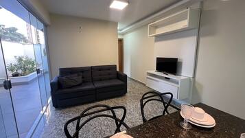 A modern living room with a dark leather sofa, a flat-screen TV on a white stand, and a dining area with a granite countertop and chairs.