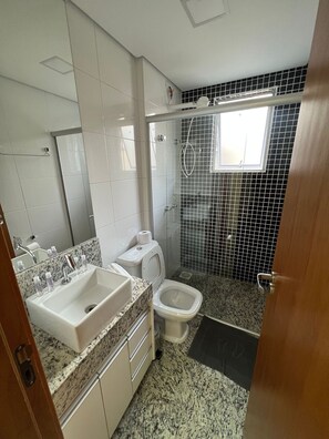 A bathroom with a white sink, toilet, and shower. The floor is covered with a speckled tile pattern. - Lockings Savassi 12 (Belo Horizonte)