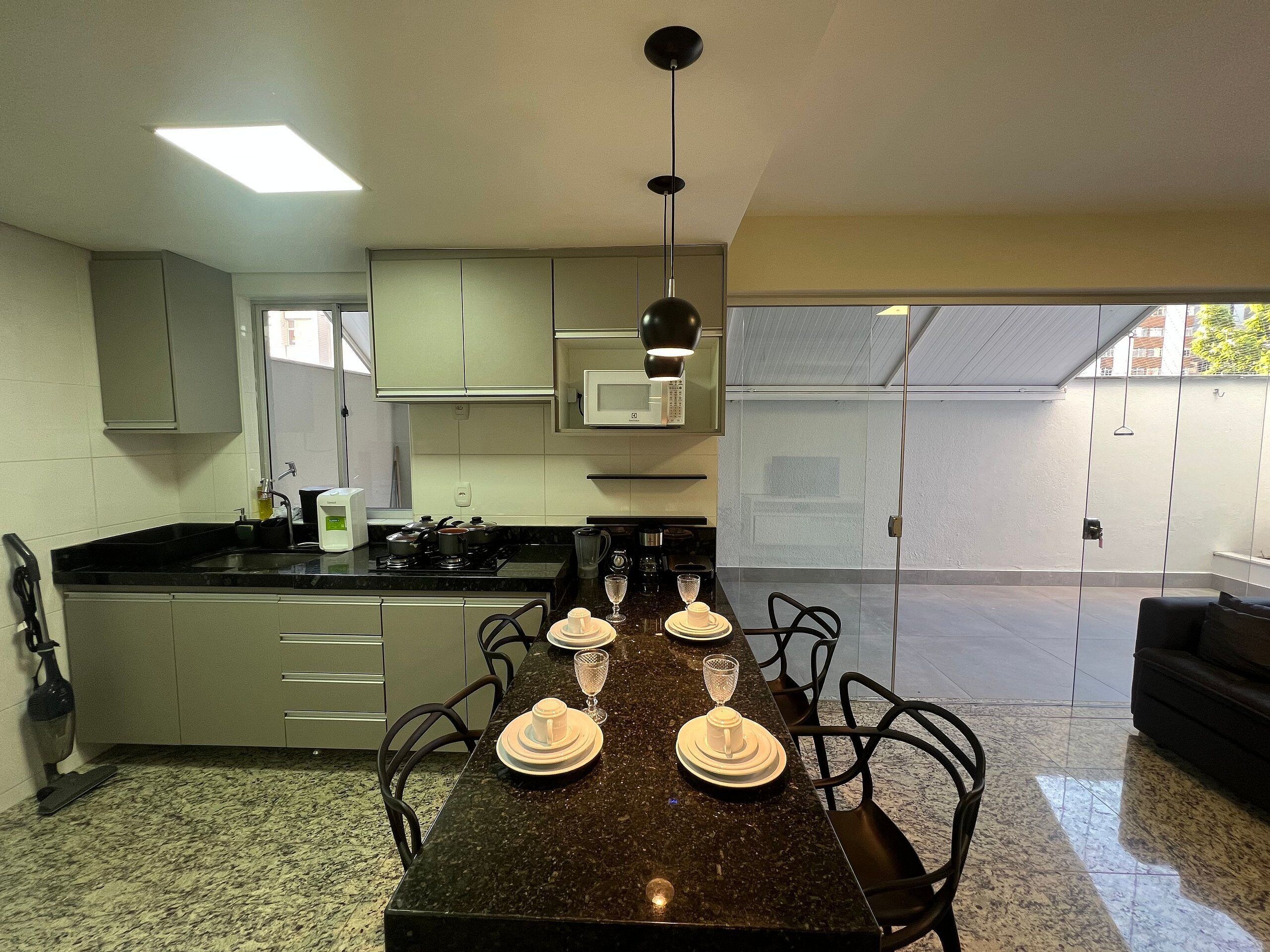 A modern kitchen with a dining table set for four, equipped with a microwave, stove, and various kitchen appliances.