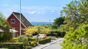 Ein rotes Haus mit geneigtem Dach, freier Meerblick und eine Windkraftanlage im Hintergrund.