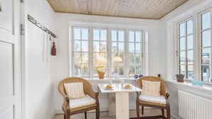 Ein gemütliches Zimmer mit zwei Korbstühlen, einem kleinen Tisch mit Tellern und Gläsern sowie einem Fenster mit Blick auf Bäume.