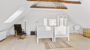 Ein Zimmer mit hohen Decken und geneigter Decke, ein weißes Bett, ein Holzstuhl, ein kleiner runder Tisch und eine Heizung.