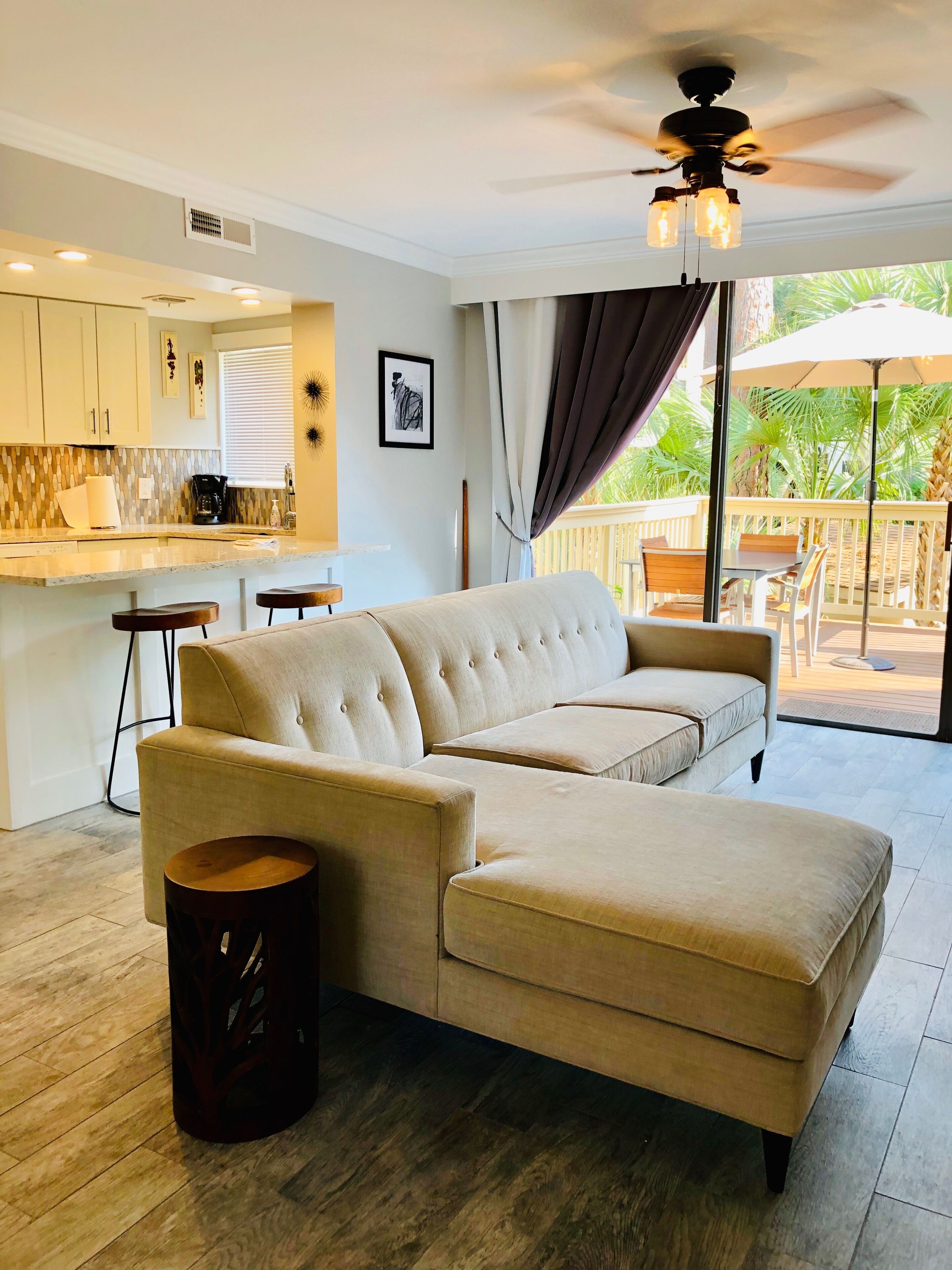 A modern living room with a beige sectional sofa, a small wooden stool, and a ceiling fan.