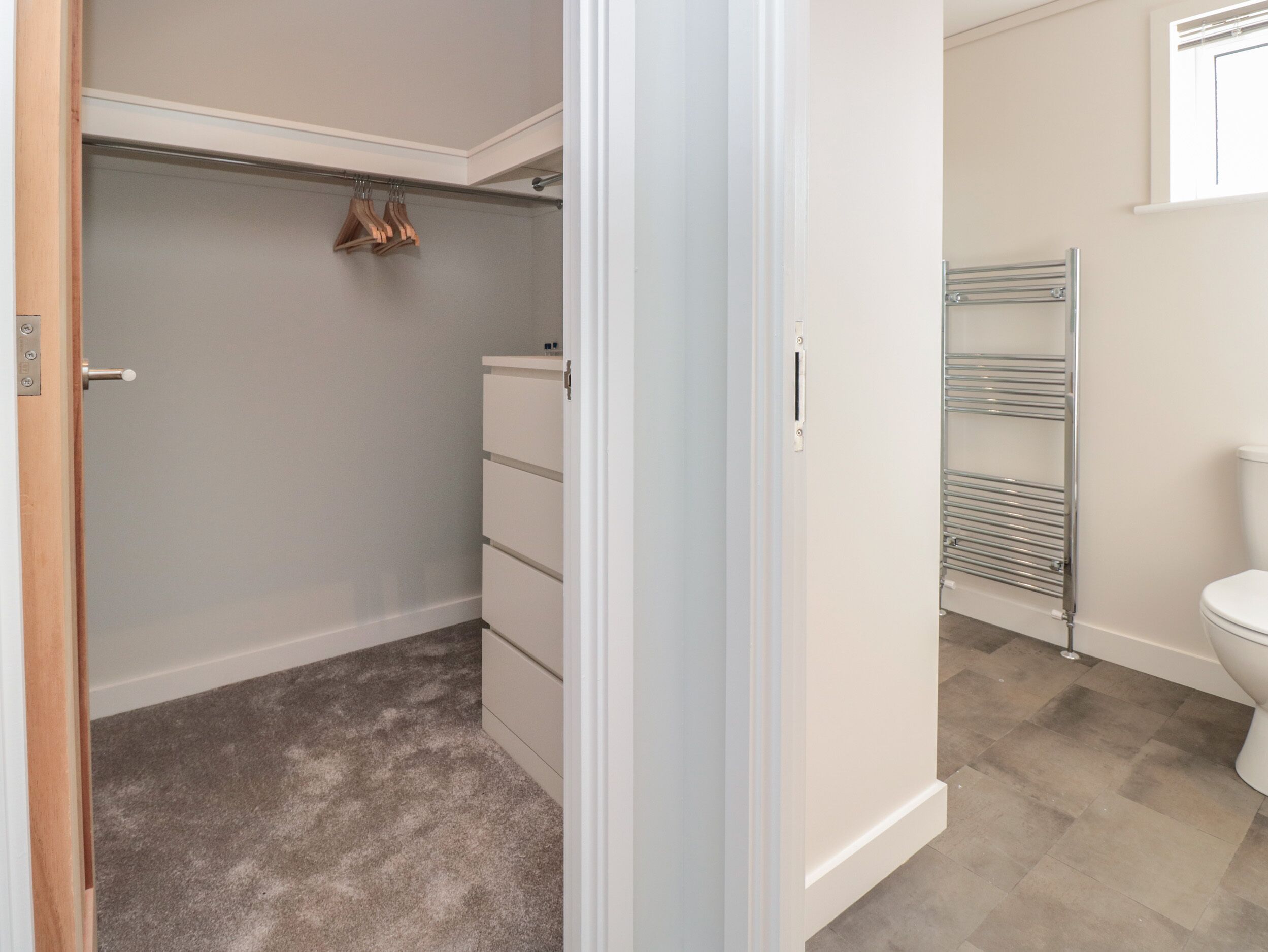 A walk-in closet with hanging space and drawers, a metal towel rack, and a toilet in a bathroom.