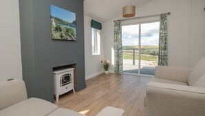 A modern living room with a fireplace, a large window with curtains, and a view of the countryside. - Primrose Lodge (Dartmouth)