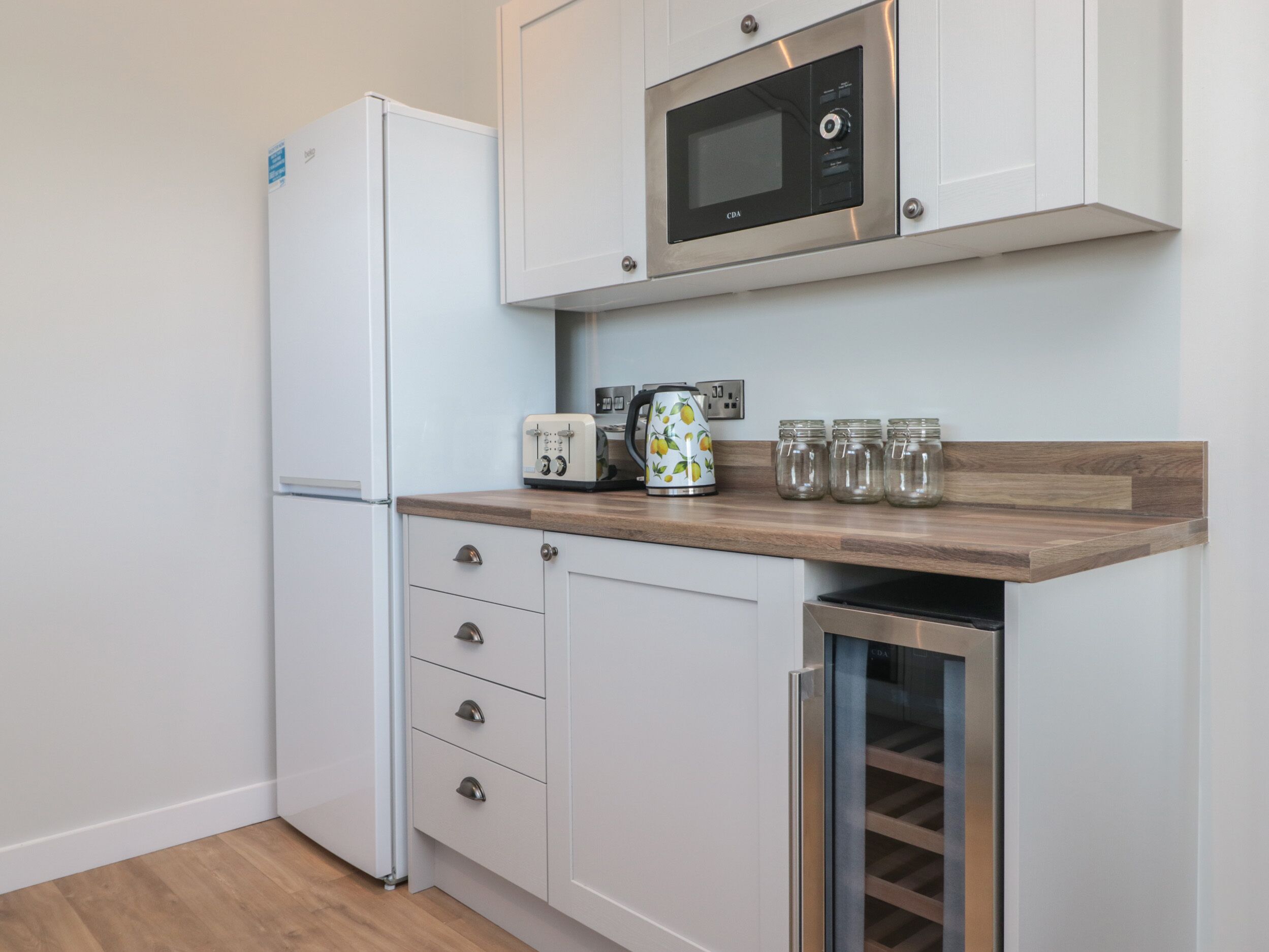 A compact kitchen with white cabinetry, a built-in microwave, a toaster, and a wine cooler.