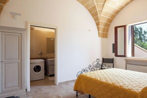 Ein Schlafzimmer mit einem Bett, einer Waschmaschine und einem durch eine offene Tür einsehbaren Badezimmer.