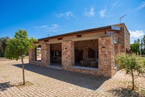 Ein Steinhaus mit offener Terrasse, Sitzgelegenheiten im Freien und blauem Himmel.